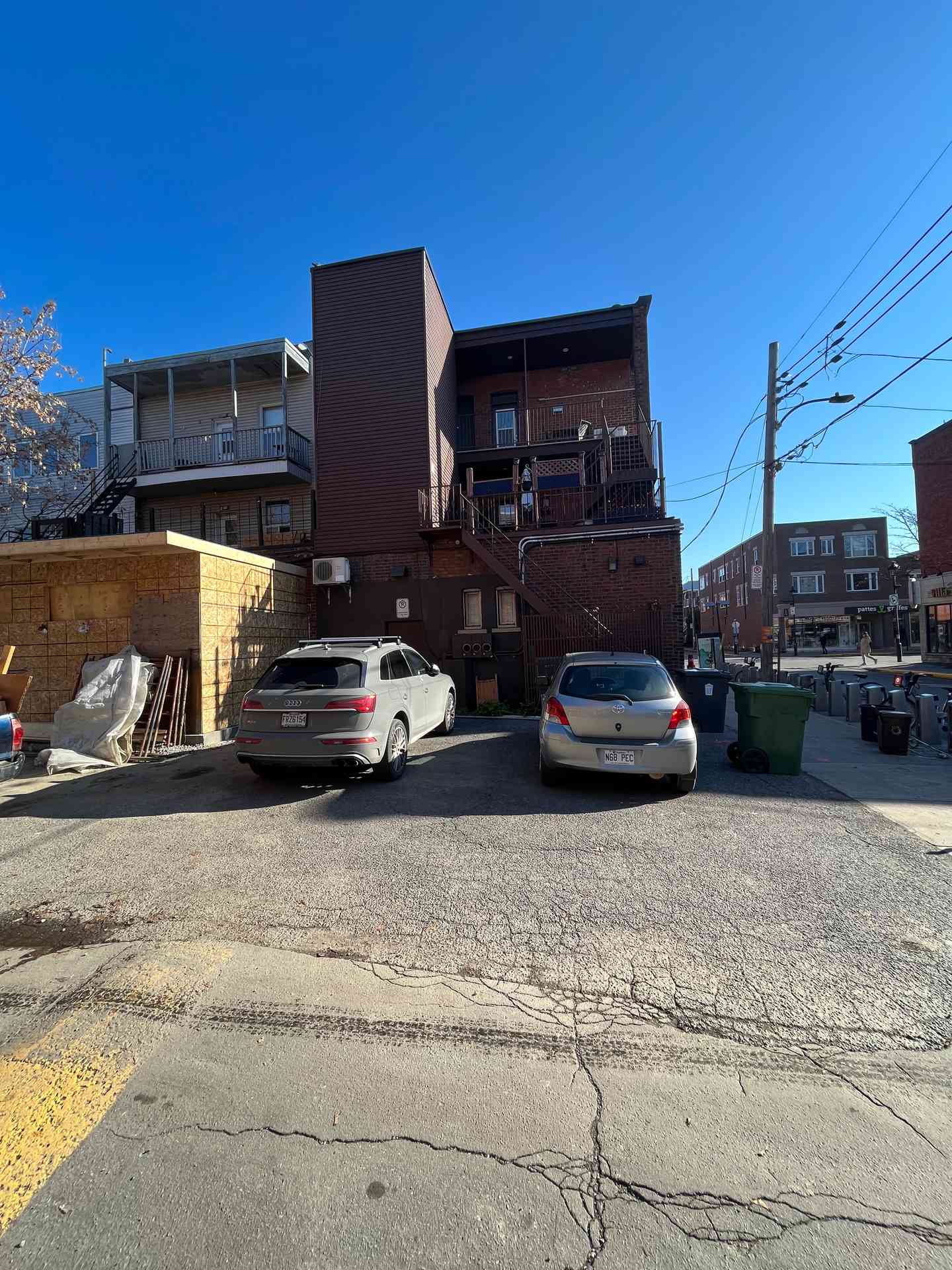Arrière du bâtiment commercial de brique vu de la ruelle, stationnement et remise de bois