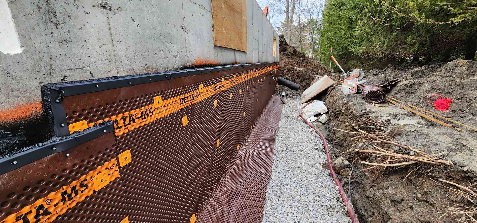 Pose de la membrane de drainage sur le mur, rouleau et gravier prêts pour le drain