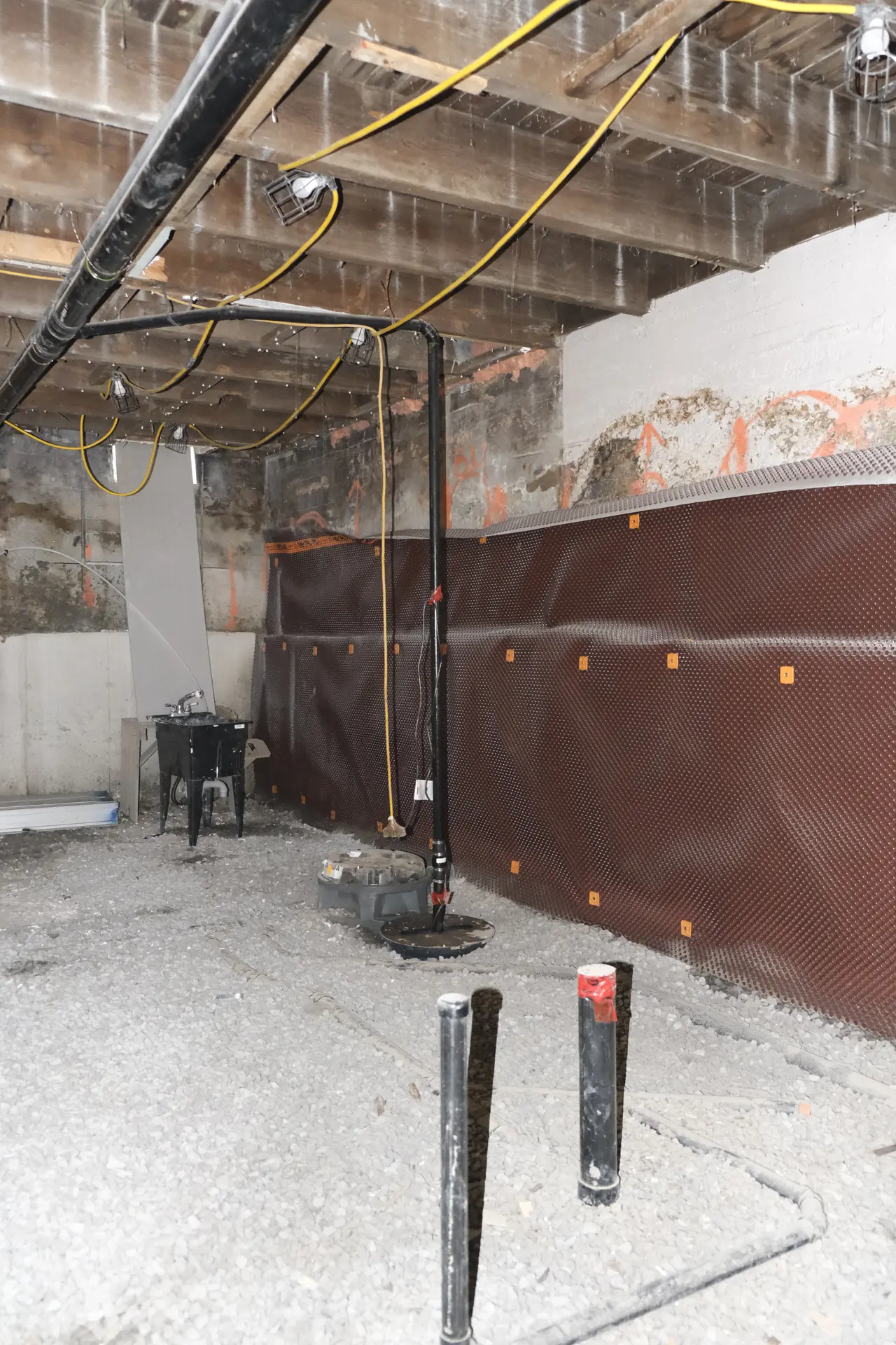 Membrane brune posée sur un mur de sous-sol et vérin d'acier appuyé sur la dalle