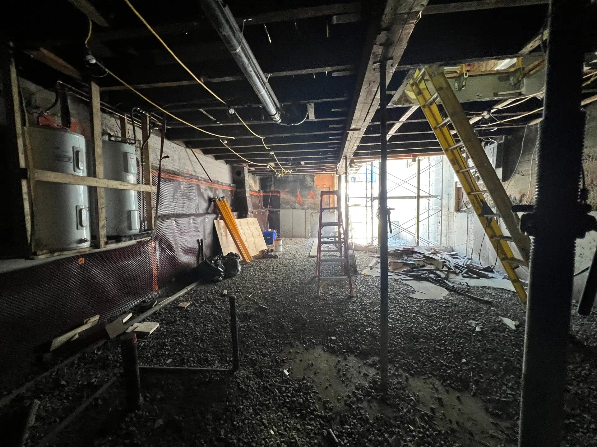Intérieur de sous-sol démoli, membrane noire au sol et plafond ouvert jusqu'aux solives