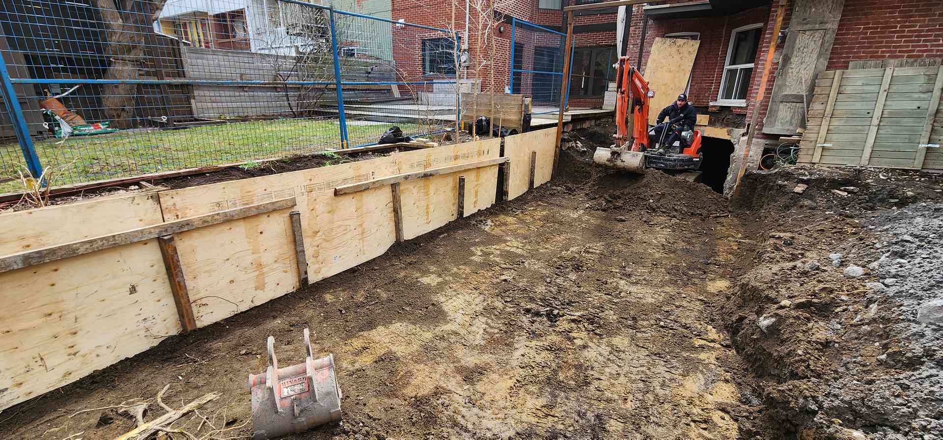Longue tranchée coffrée de bois le long d'un bâtiment avant le coulage de la fondation