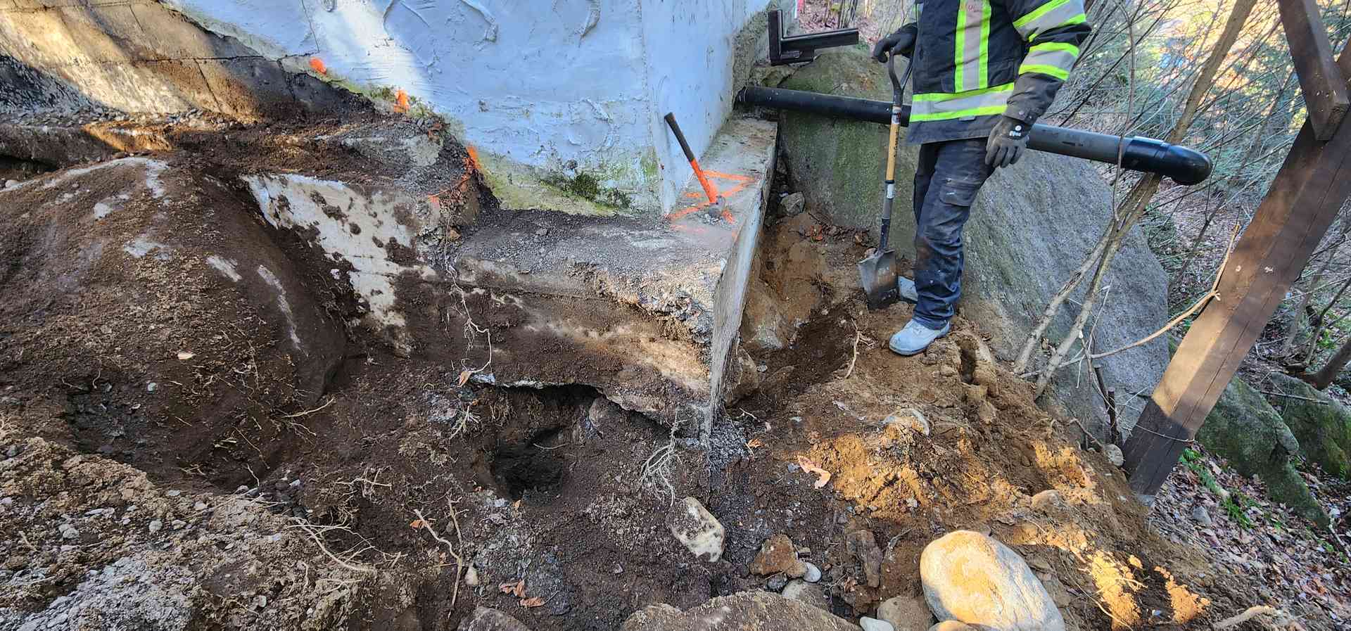 Ouvrier dégageant à la barre un bloc de béton fracturé au fond de l'excavation