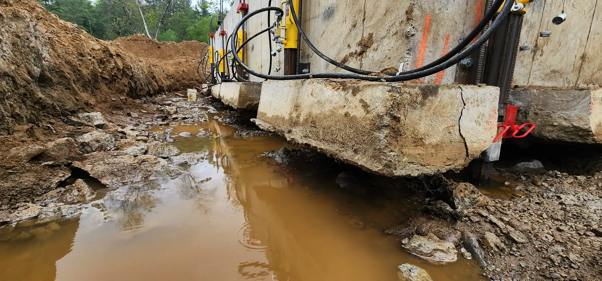 Section de mur de fondation soutenue par des vérins au-dessus d'une tranchée remplie d'eau
