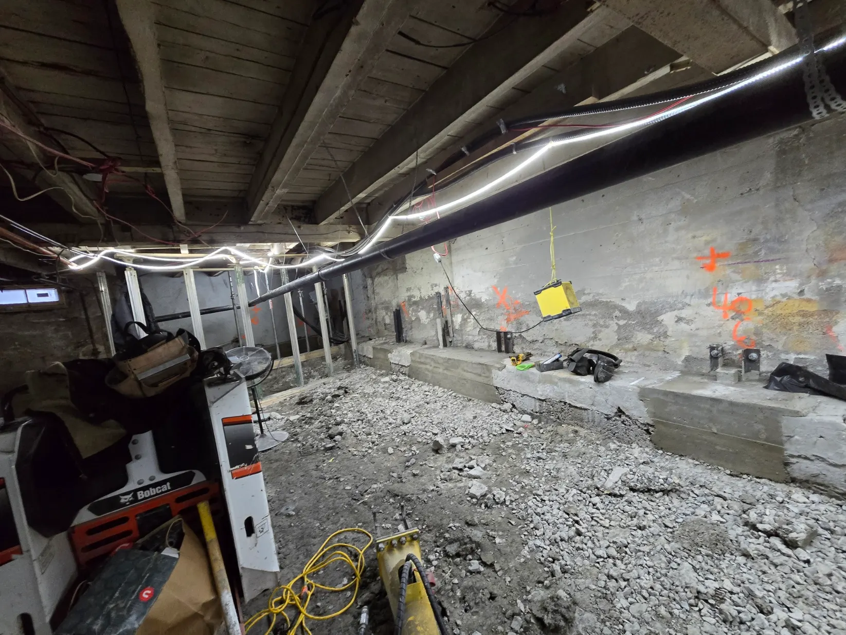 Sous-sol en chantier : solives apparentes, conduits et équipement près du mur de béton