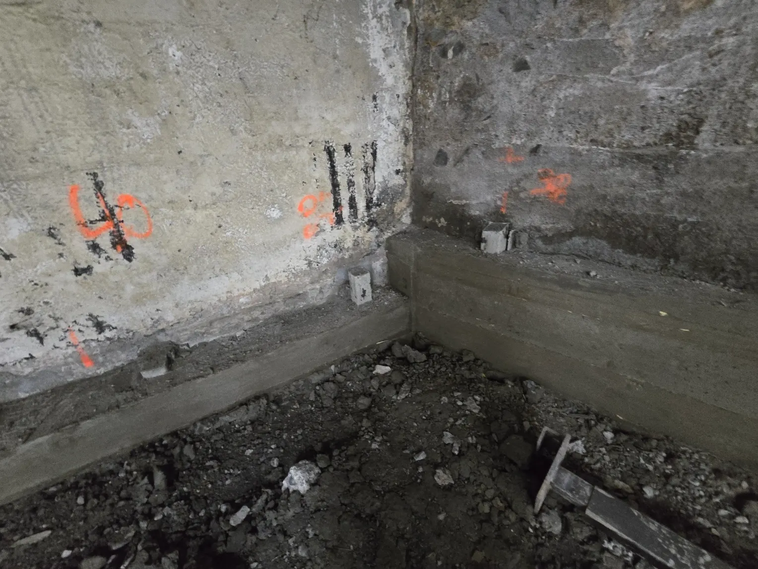 Coin de mur de fondation marqué à l'orange, ancrages d'acier posés au-dessus du sol de terre