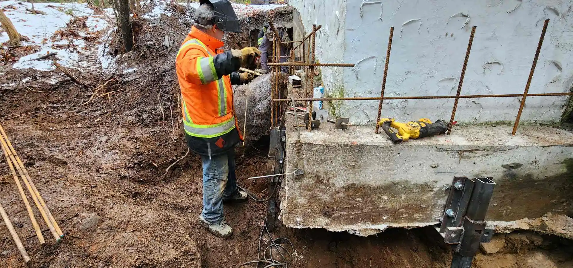 Ouvrier en dossard perçant un mur de fondation, armature d'acier dressée dans la tranchée