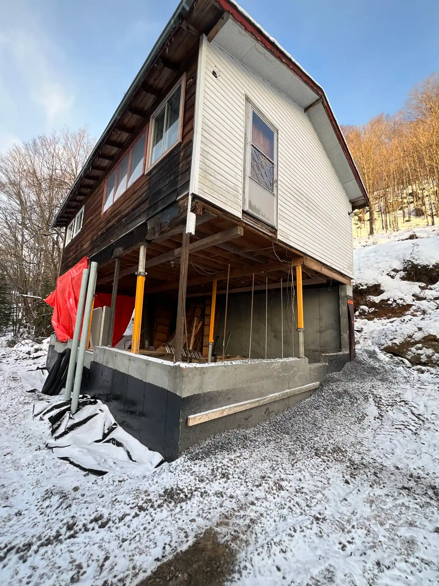 Nouveau mur de fondation coulé sous la maison, bâche rouge et étais encore en place