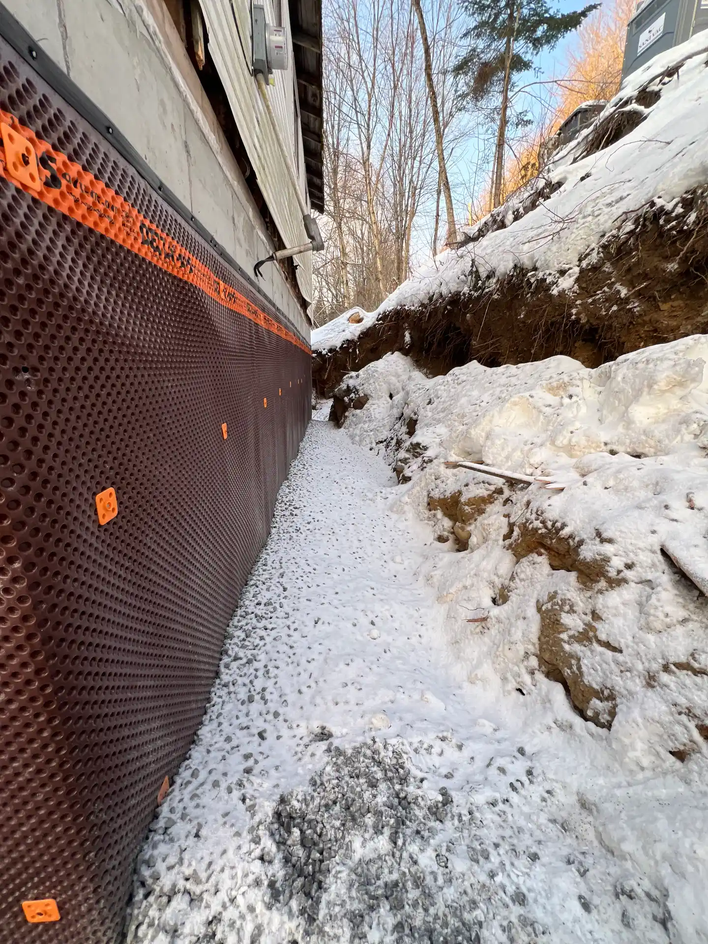 Membrane de drainage alvéolée noire posée contre le nouveau mur de fondation