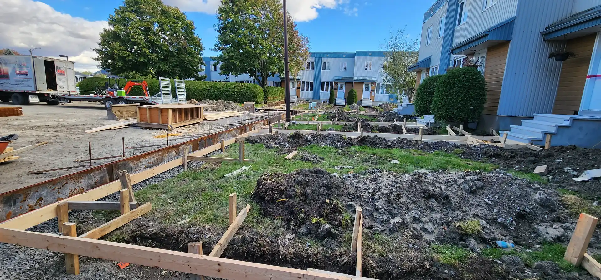 Trottoir de béton | Stabili Pieux Coffrages alignés dans une cour excavée avec monticules de terre devant des logements